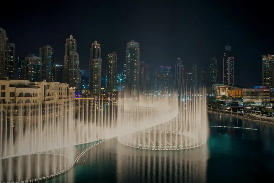 The Dubai Fountain lit at night in front of the Downtown towers